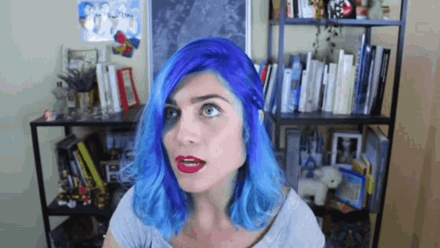 a woman with blue hair stands in front of a book shelf
