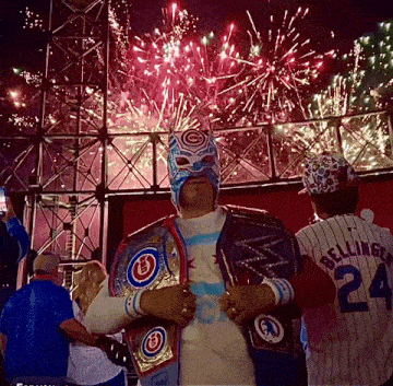 a man wearing a mask and a chicago cubs shirt stands in front of fireworks