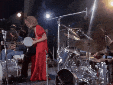 a woman in a red dress plays a drum on stage