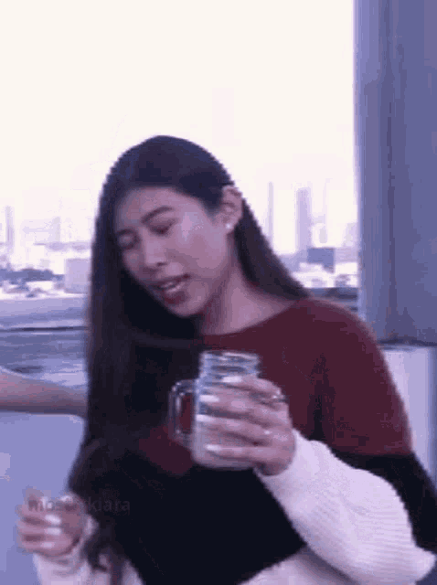 a woman is sitting on a balcony holding a mason jar of milk .