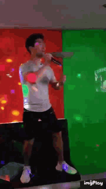 a man is singing into a microphone in front of a green and red wall