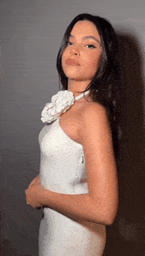 a woman is wearing a white dress with a flower on her neck
