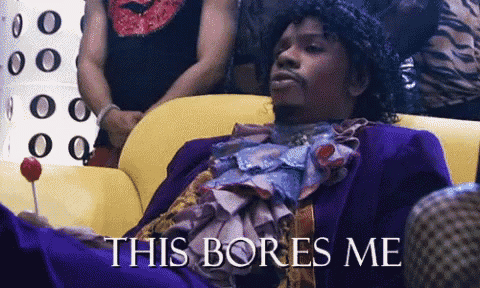 a man in a purple suit is sitting on a yellow couch and holding a lollipop with the words this bores me below him