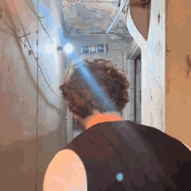 a man in a black tank top stands in a hallway with a green exit sign on the wall