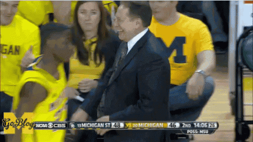 a man wearing a yellow shirt with the letter m on it sits in the stands
