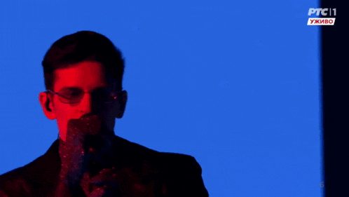 a man wearing glasses and a turtleneck stands in front of a blue background with ptc11 written on it