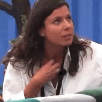 a woman in a white shirt is sitting in front of a blue curtain and holding her chest .
