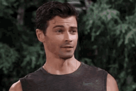 a man in a black tank top is standing in front of a tree and smiling .