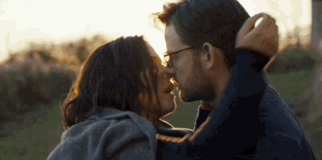 a man and a woman are kissing in a field with the sun shining through their eyes .