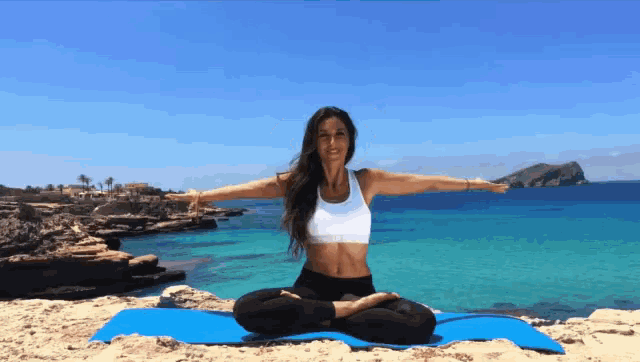a woman sits on a yoga mat with her arms outstretched