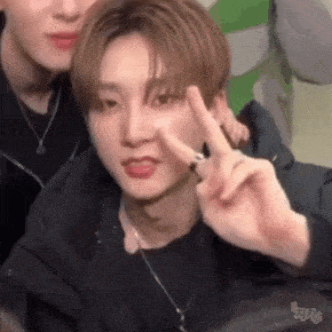 a young man is making a peace sign with his fingers while sitting next to another young man .