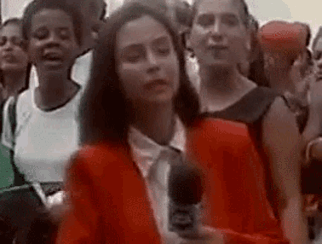 a woman in a red suit is holding a microphone in front of a crowd of people .