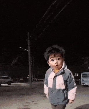 a little boy in a jacket is making a funny face in a parking lot at night .