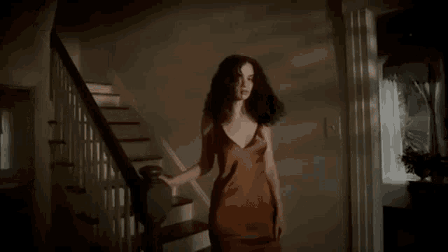 a woman in a brown dress is walking down a set of stairs in a dark room .