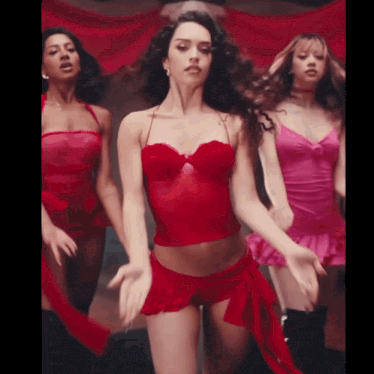 a woman in a red top and shorts is dancing with two other women in pink lingerie .