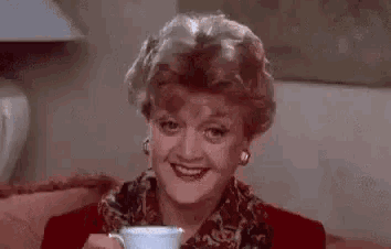 a woman is drinking a cup of tea and smiling .