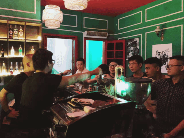 a group of people are gathered at a bar with green walls and bottles on the shelves