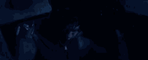 a man is standing in a dark room with a brick behind him .