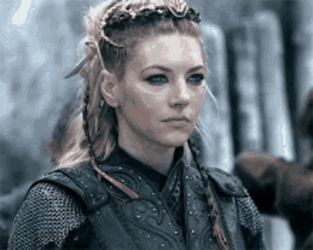 a woman with braids and a crown on her head is wearing chain mail and a black vest .