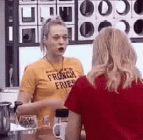 two women are standing next to each other in a kitchen talking to each other .