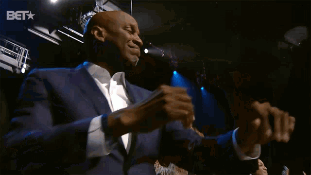 a man in a suit and white shirt is dancing in front of a bet sign