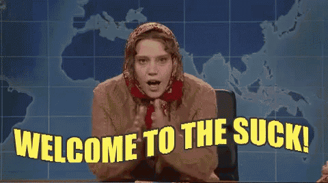 a woman in a scarf is sitting at a desk with the words welcome to the suck behind her