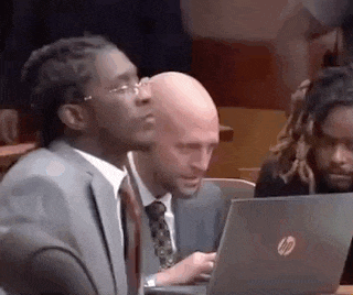 a man in a suit and tie is sitting in a courtroom looking at a laptop .