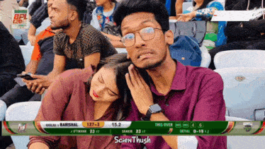 a man and a woman are sitting in a stadium watching a cricket game and the scoreboard says scientifichush