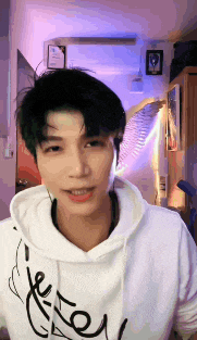 a young man wearing headphones and a white hoodie is smiling while looking at the camera .