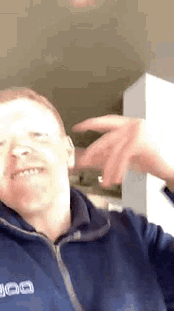 a man in a blue jacket is making a funny face and pointing at the camera .