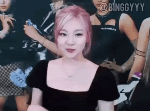 a woman with pink hair and a black dress is standing in front of a group of women .