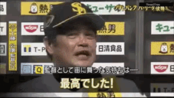 a man in a baseball cap is talking in front of a wall of advertisements for nissin