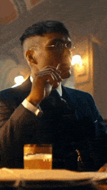 a man in a suit smoking a cigarette and drinking a glass of beer