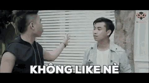 two men are standing next to each other in front of a window and talking .