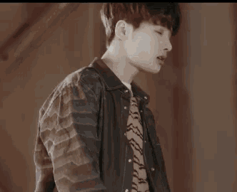 a young man in a plaid shirt and a leather jacket is standing in a dark room .