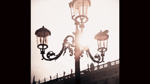 a black and white photo of a lamp post with the sun shining through it