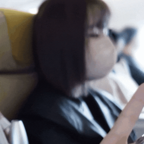 a woman wearing a mask sits on a plane looking at her phone