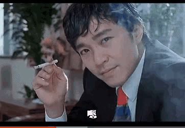 a man in a suit and tie is smoking a cigarette while looking at the camera .