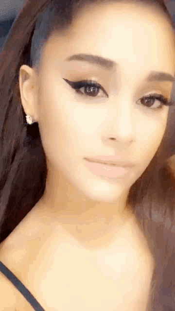 ariana grande is wearing a black tank top and earrings while taking a selfie .