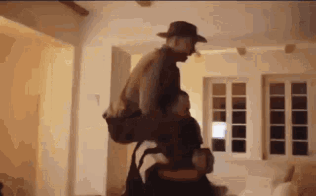 a man in a cowboy hat is riding on the back of another man in a living room .