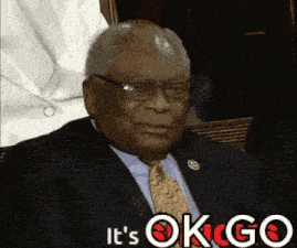 a man in a suit and tie is sitting in front of a sign that says " it 's ok go "
