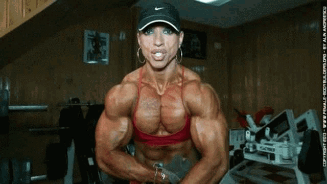 a very muscular woman is in a gym with a nike hat on