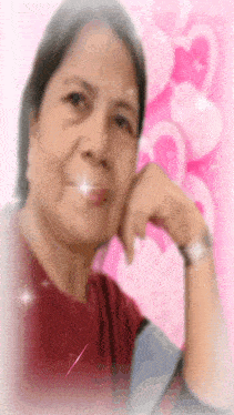 a woman with her hand on her chin is standing in front of a pink background with hearts .