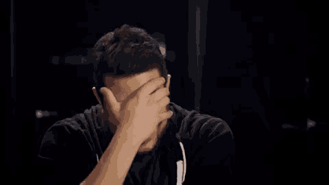 a man in a black shirt is covering his face with his hands .