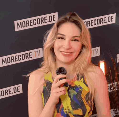 a woman is holding a microphone in front of a morecore.de sign