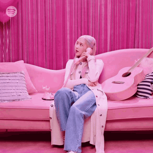 a woman sits on a pink couch talking on a phone