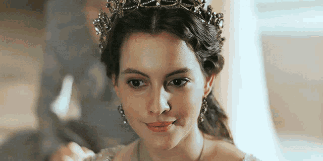 a woman wearing a tiara and earrings looks at the camera