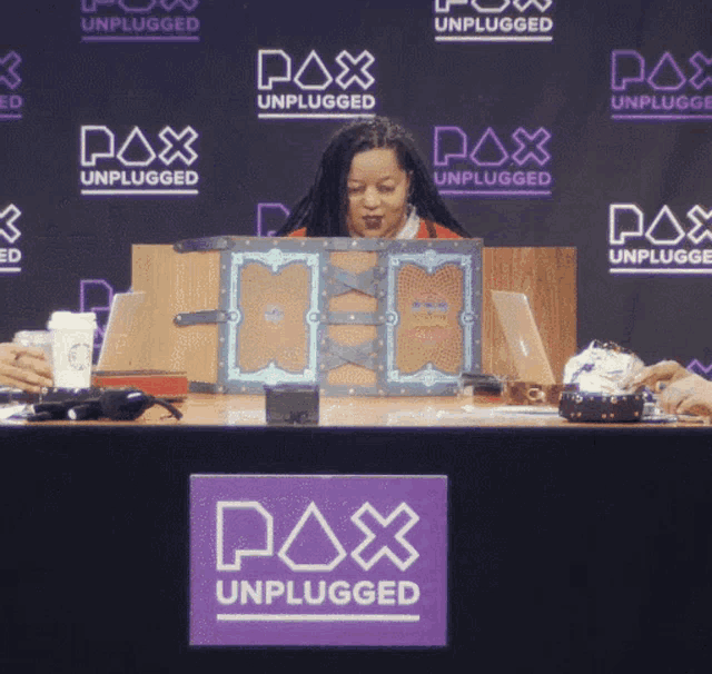 a woman sits at a desk in front of a pax unplugged sign