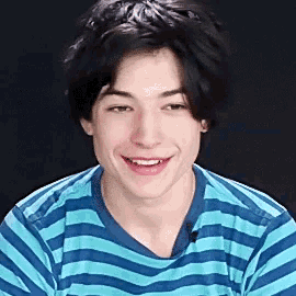 a young man wearing a blue and white striped shirt is smiling and looking at the camera .
