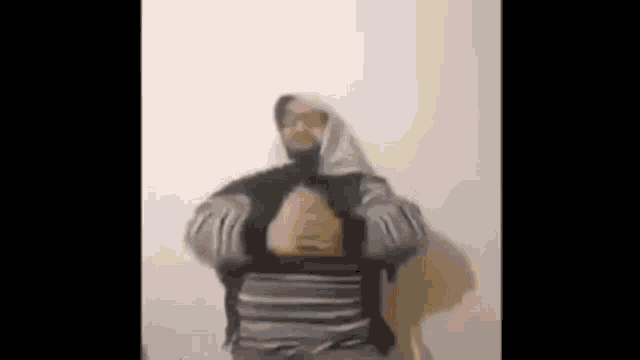 a man wearing a head scarf and a striped shirt is standing in front of a wall .